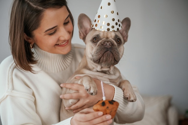 Célébration d'anniversaire avec des chapeaux et du gâteau Une jeune femme est avec son chiot à la maison