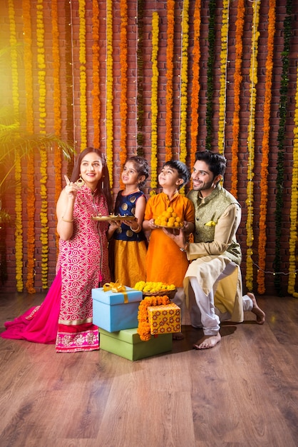 Célébration Diwali ou Rakshabandhan - Jeune famille indienne de quatre personnes célébrant le festival Deepavali ou bhai Dooj avec un doux laddoo, une lampe à huile ou un diya et des coffrets cadeaux, mangeant de la nourriture ou prenant un selfie
