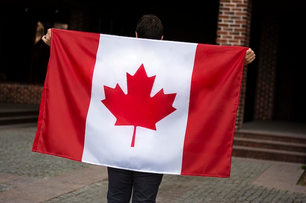 Célébration du drapeau de la fête du Canada entre les mains d'un bel homme sur fond de rue de la ville