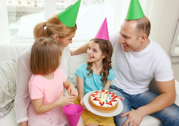 célébration, famille, vacances et concept d'anniversaire - famille heureuse avec deux enfants en chapeaux avec gâteau à la maison