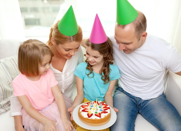célébration, famille, vacances et concept d'anniversaire - famille heureuse avec deux enfants en chapeaux avec gâteau à la maison