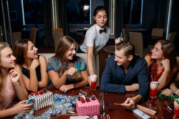 Célébration de la fête du nouvel an. Fond de boîte de nuit. Entreprise joyeuse avec boissons et serveuse. Des gens souriants à Noël, de jolies décorations