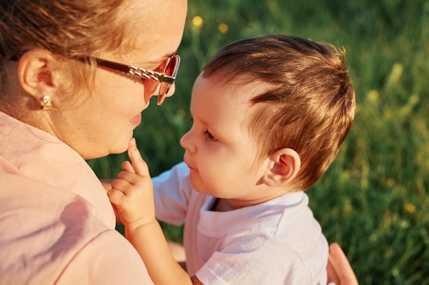 Photo célébration de la fête des mères close-up d'une jeune mère avec sa petite fille assise dans un champ vert sur de l'herbe verte en train de s'embrasser en profitant d'un moment heureux ensemble en plein air dans la nature