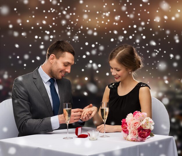 célébration, noël, vacances et concept de personnes - couple souriant avec boîte-cadeau rouge et anneau au restaurant sur fond de ville de nuit enneigée