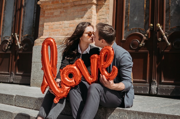 Célébration de la Saint-Valentin et concept de rencontres. Heureux couple d'amoureux avec des ballons d'amour rouges dans la rue de la ville. Portrait en plein air de jeune couple avec ballon en forme de mot amour.