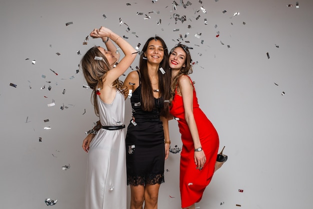Célébrer les amis de jeunes filles portant des robes de soirée serrant sous des confettis argentés en fête sur fond gris