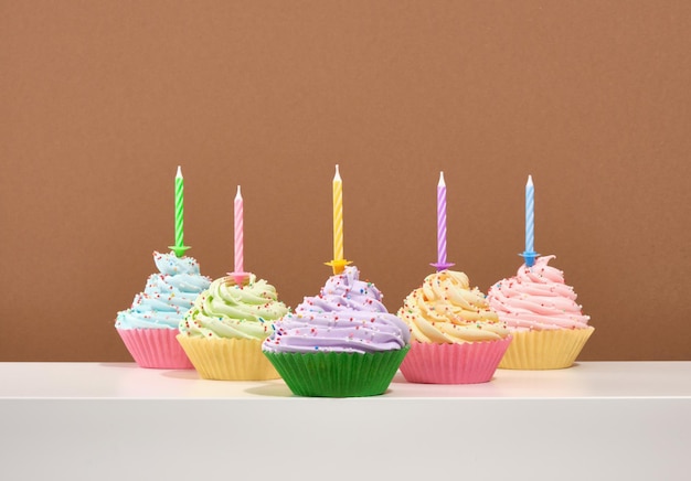 Célébrer des cupcakes lumineux avec différentes crèmes sucrées délicieuses et des bougies festives sur une table blanche Composition de cupcakes délicieux et week-ends