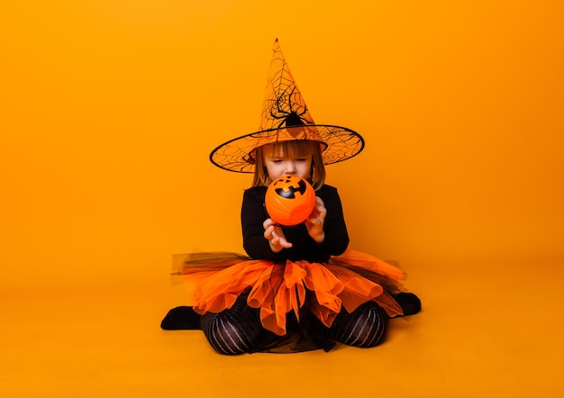 Célébrer Halloween. Petite fille habillée en sorcière tient un seau de citrouilles sur fond jaune.