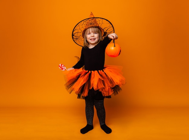 Célébrer Halloween. Petite fille habillée en sorcière tient un seau de citrouilles sur fond jaune.