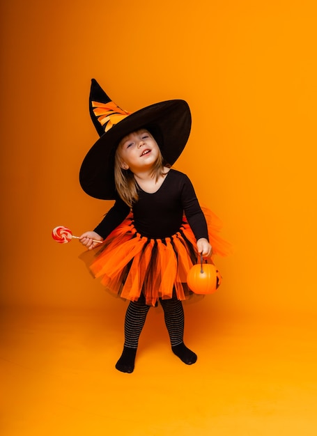 Célébrer Halloween. Petite fille habillée en sorcière tient un seau de citrouilles sur fond jaune.