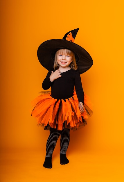 Célébrer Halloween. Petite fille habillée en sorcière tient un seau de citrouilles sur fond jaune.