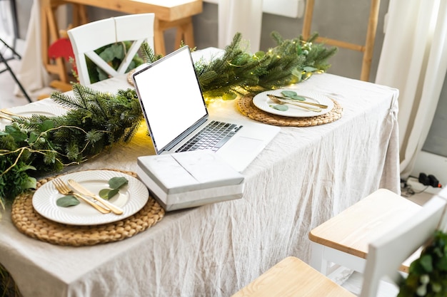 Célébrer joyeux noël et nouvel an à la maison, bougies et guirlandes, ordinateur portable sur la table dans la cuisine.