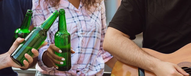 Célébrer. Mains d'amis, collègues pendant qu'ils boivent de la bière, s'amusent, font tinter des bouteilles, des verres ensemble.