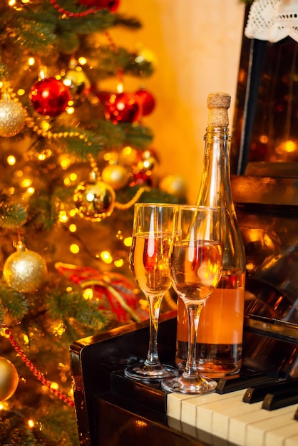 Célébrer Noël avec du champagne Deux verres de champagne ou de vin et une bouteille au piano près d'un arbre de Noël décoré, le tout dans des lumières vives