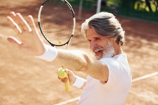 Célébrer la victoire Senior homme élégant moderne avec une raquette à l'extérieur sur un court de tennis pendant la journée