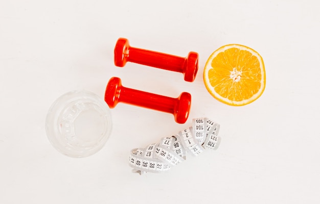 Un centimètre, une orange, un verre d'eau et des haltères rouges. Concept de soins de santé, d'alimentation et de sport