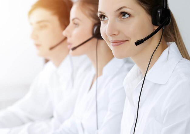 Centre d'appel. Belle jeune femme utilisant un casque et un ordinateur pour aider les clients dans un bureau ensoleillé. Notion d'entreprise.