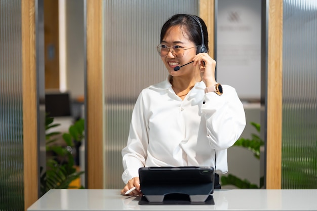 Photo centre d'appels affaires attrayantes femme asiatique utilisant des casques travaillant avec une tablette numérique chez des agents de service à la clientèle de télémarketing