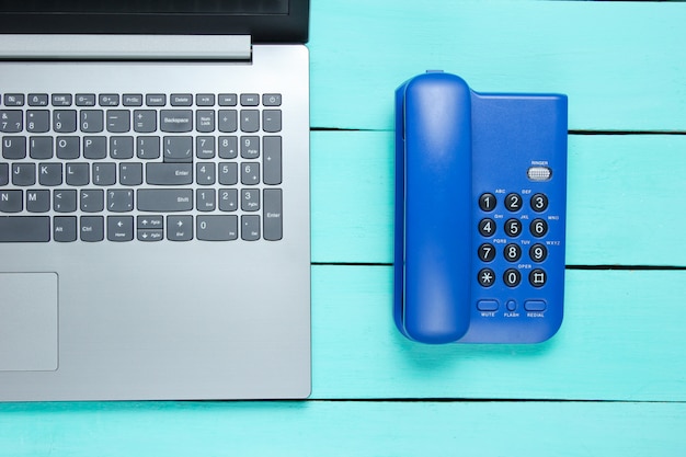 Centre d'appels de l'espace de travail. Ordinateur portable, téléphone de bureau sur une table en bois bleue.