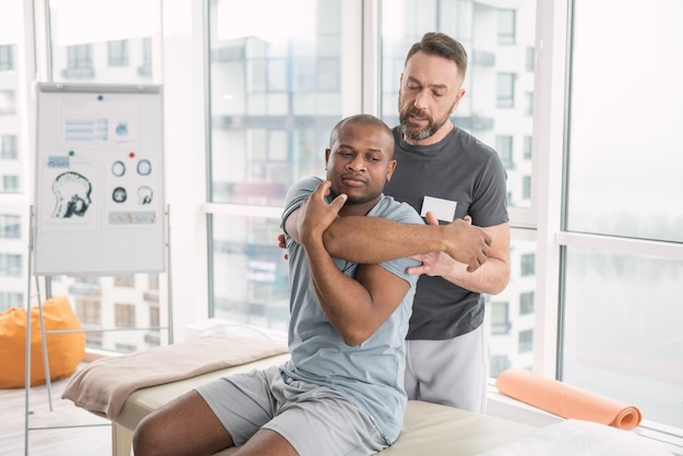 Centre de santé. Sérieux jeune homme bougeant ses mains tout en essayant de développer ses muscles