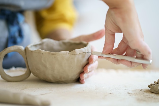 Le céramiste artisanal au travail utilise des outils pour créer une tasse à la main en studio gros plan sur des mains de potier féminin