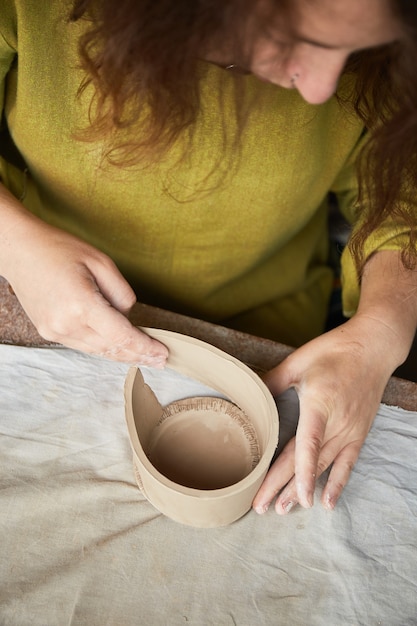 Photo céramiste travaillant dans un atelier de poterie. les mains du céramiste sales d'argile. processus de création de poterie. maître céramiste travaille dans son atelier