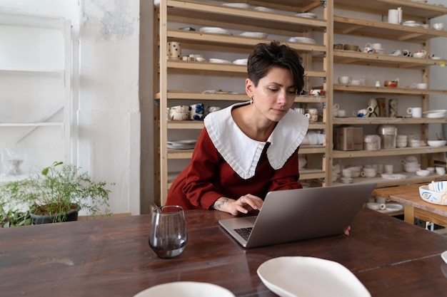 Céramiste travaillant sur un ordinateur portable dans un magasin de céramique ou un studio d'art vendant de l'art sur les réseaux sociaux