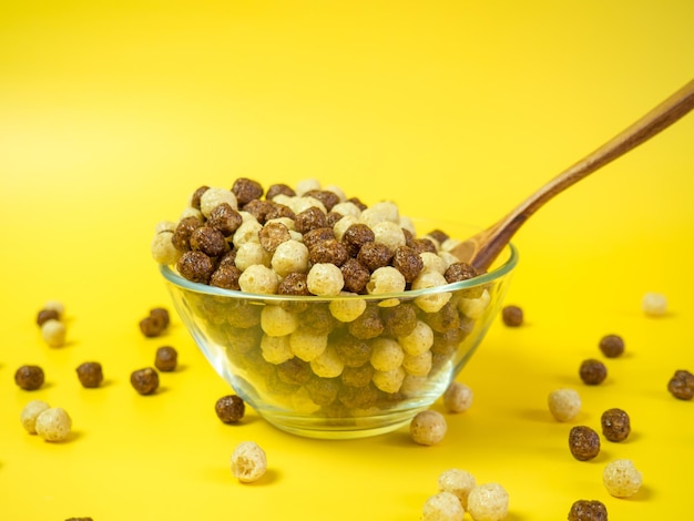 Céréales pour petit-déjeuner Vanille et boules de maïs au chocolat dans un bol en verre sur fond jaune