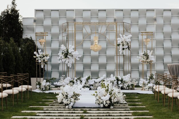 Une cérémonie de mariage avec un arrangement floral blanc et des murs d'or et d'argent.