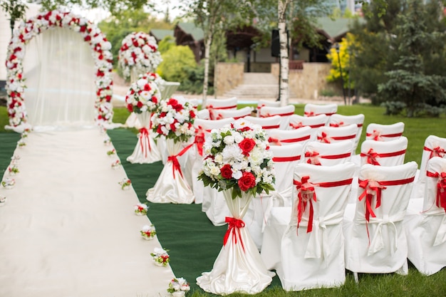 Cérémonie de mariage en plein air avec des chaises blanches et des rubans rouges