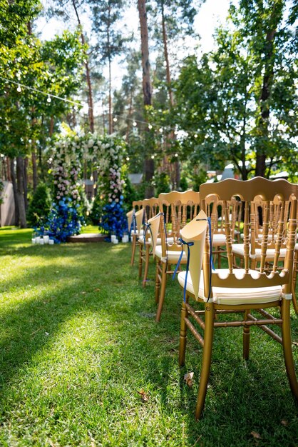 Cérémonie de mariage en plein air sur une pelouse verte. Arche pour une cérémonie de mariage de fleurs fraîches en blanc et bleu et chaises en or pour les invités. Mise au point sélective douce.