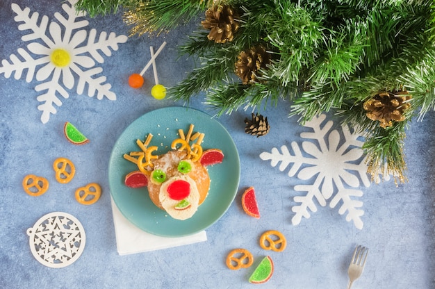 Cerf comestible de Noël de brioches et de marmelade sur une plaque bleue sur la table de vacances à côté de bonbons