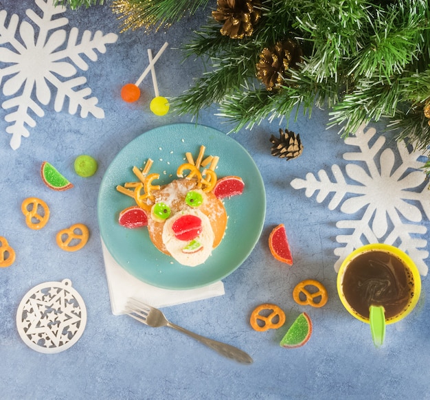 Cerf comestible de Noël de brioches et de marmelade sur une plaque bleue sur la table de vacances à côté de bonbons