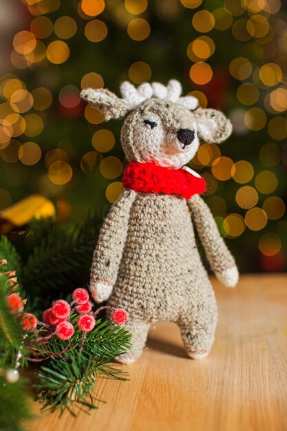 Le cerf jouet au crochet de couleur grise se tient sur une table en bois avec une branche d'arbre de Noël à proximité