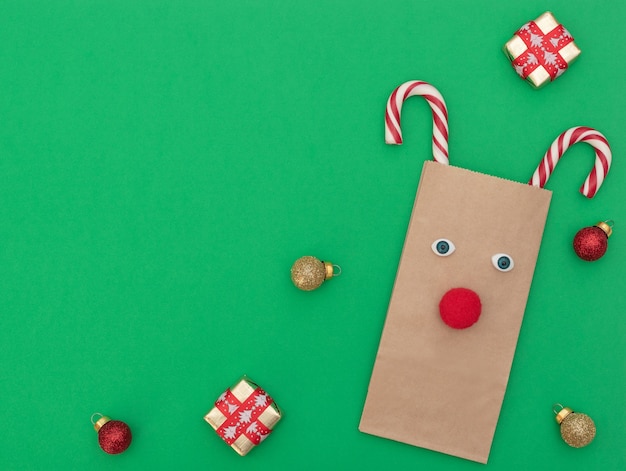 Cerf de Noël en sac à provisions artisanal et deux cannes de Noël avec coffrets cadeaux et boules de Noël sur fond vert. Style plat avec espace de copie.