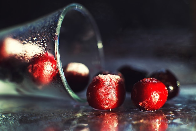 Cerise congelée en gros plan dans le verre avec reflet cerise congelée sur une macro de fond sombre