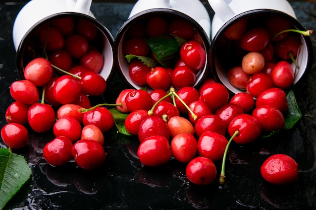 Cerise dispersée dans des tasses en émail. Cerises dans une tasse en fer sur fond noir. Fruits d'été sains. Cerises. Trois. Fermer.