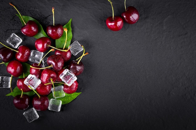 Cerise avec des feuilles et des gouttes d'eau sur une table en pierre noire.