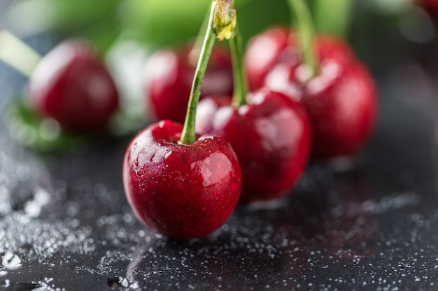 Cerise fraîche avec des gouttes d'eau sur une table sombre.