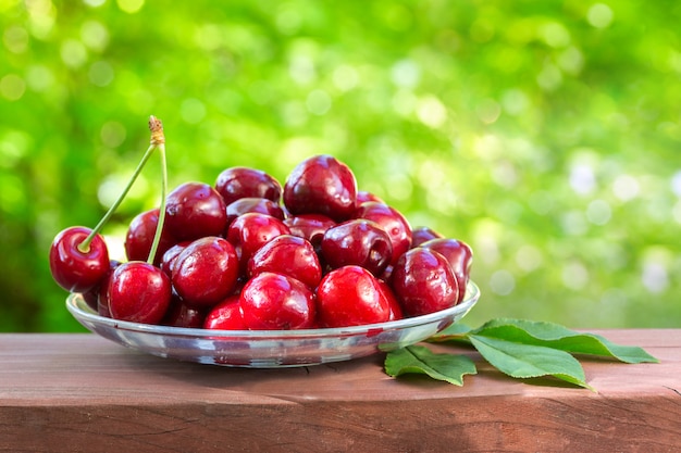 Cerise sur un plateau en verre sur la verdure. Belle journée ensoleillée. Fruits juteux, savoureux et sains.