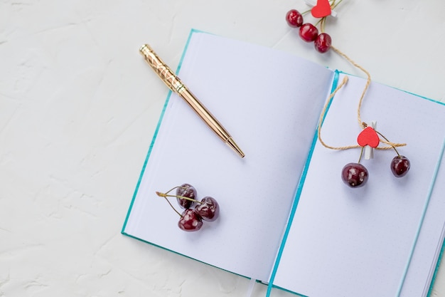 Cerises douces, coeur rouge et carnet de notes avec un stylo doré.