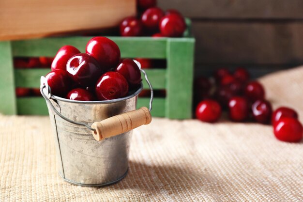 Cerises douces avec des feuilles vertes dans un seau et des caisses en bois sur fond de bois