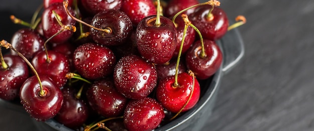 Cerises douces fraîches avec des gouttes d'eau dans un bol sur une table de roche sombre.