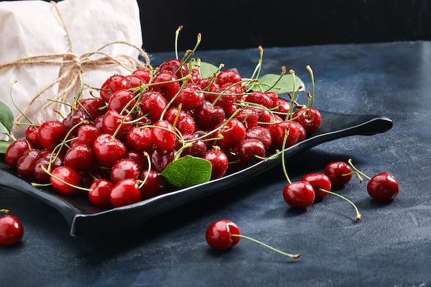 Cerises douces fraîches sur une plaque sur un fond bleu. Concept de baies fraîches, livraison de nourriture, emballage écologique