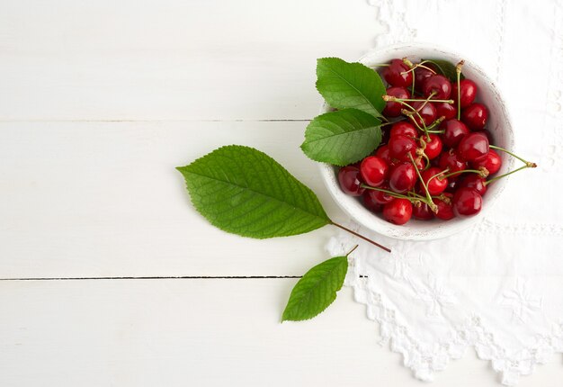 Cerises douces rouges mûres dans une assiette en bois ronde sur fond blanc, vue du dessus