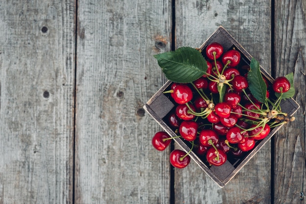 Cerises avec des feuilles dans une boîte en bois vintage sur table en bois rustique. Copiez l'espace.