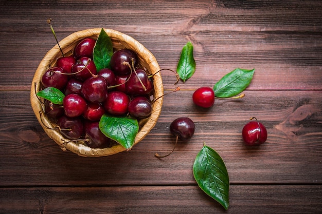 Cerises avec des feuilles dans un panier sur un fond en bois