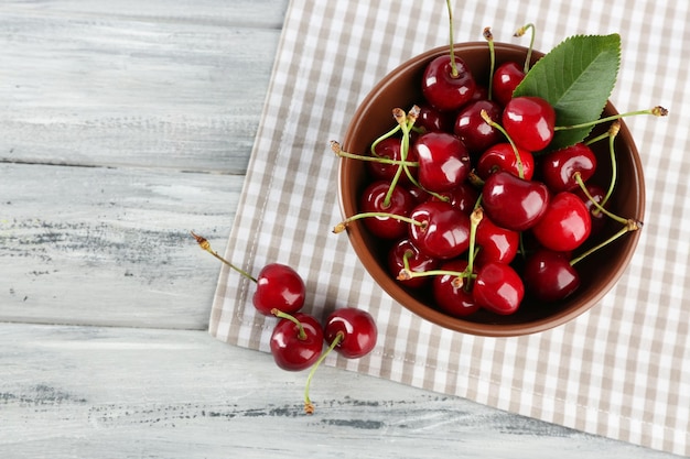 Cerises fraîches dans un bol avec une serviette sur une table en bois agrandi