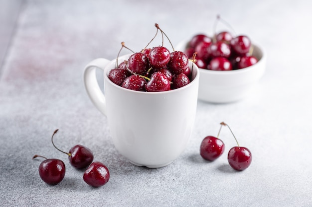 Cerises fraîches dans une tasse blanche sur fond de pierre grise