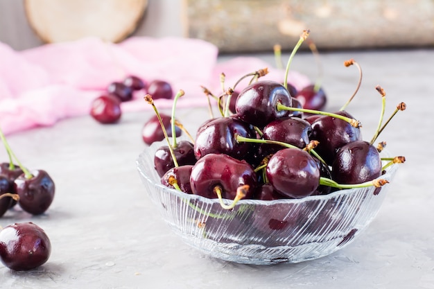 Cerises fraîches mûres dans un bol en verre sur fond gris